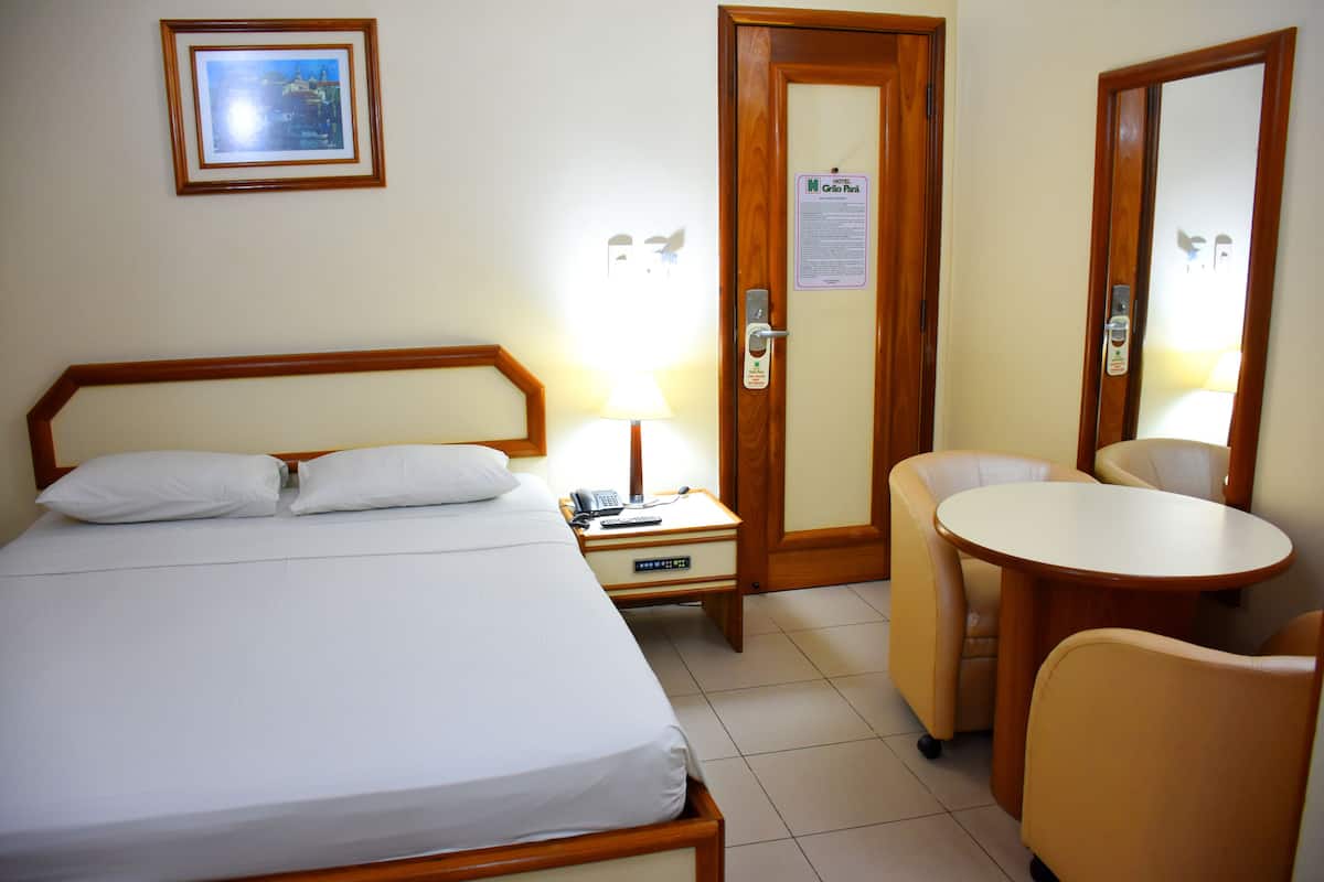 Una habitación de hotel con cama, mesita de noche, lámpara, silla y una pequeña mesa.