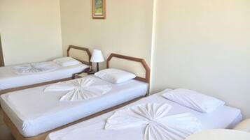 A hotel room with three single beds, each with a neatly folded white blanket and a wooden headboard.