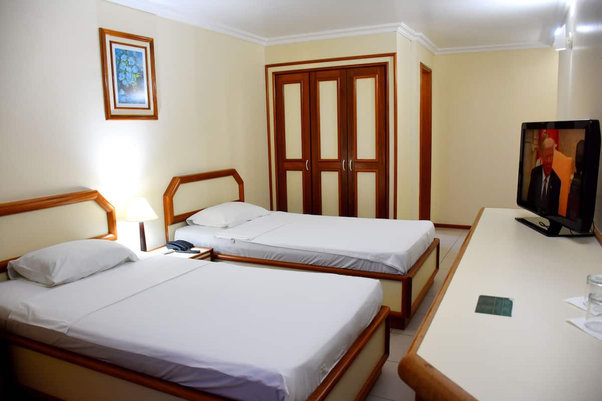 Habitación de hotel con dos camas individuales, un armario de madera, un televisor y un escritorio con una silla.