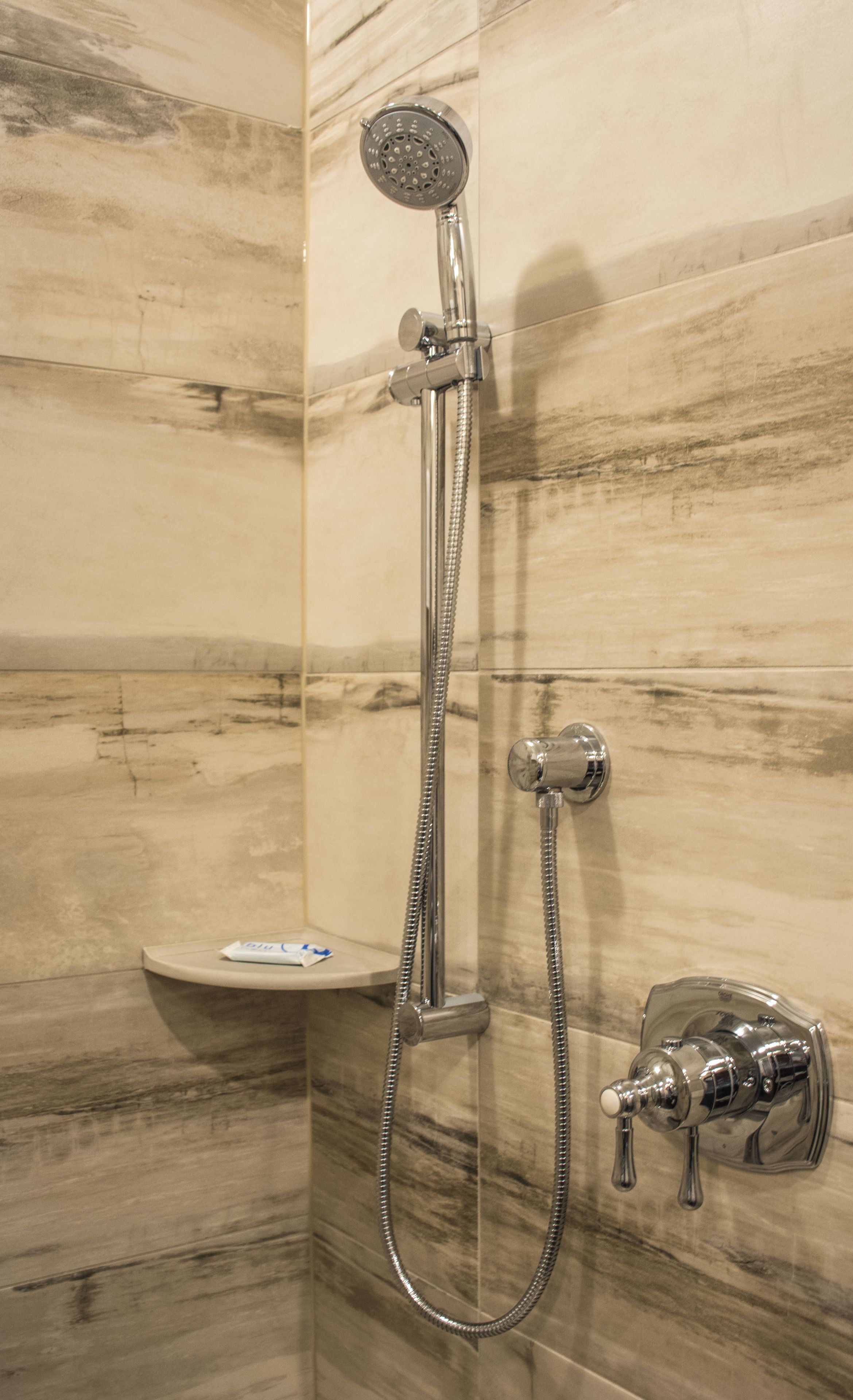 A shower with a handheld showerhead and a wall-mounted faucet, set against a marble wall.
