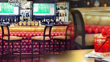A bar area with multiple bar stools, a red upholstered bench, and a glass of red drink with a straw.