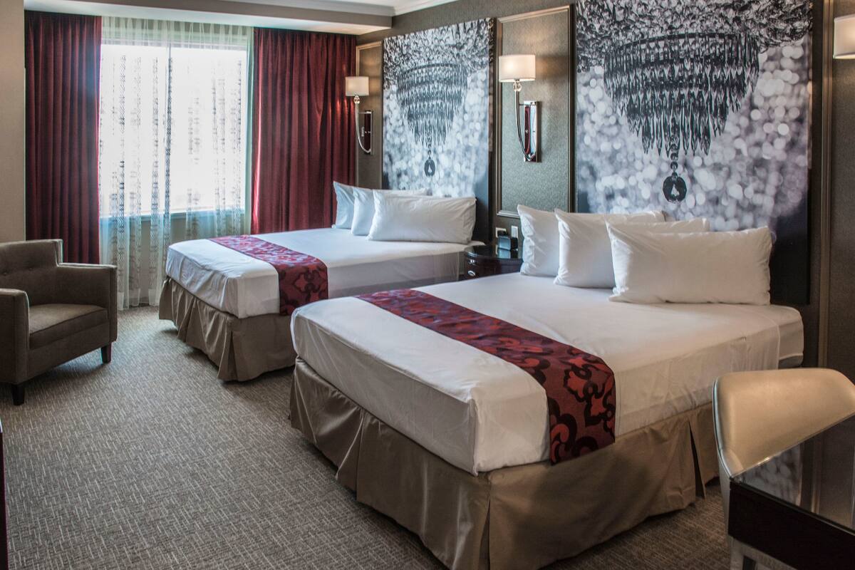 A hotel room with two beds, a desk, a chair, and a large tapestry on the wall.