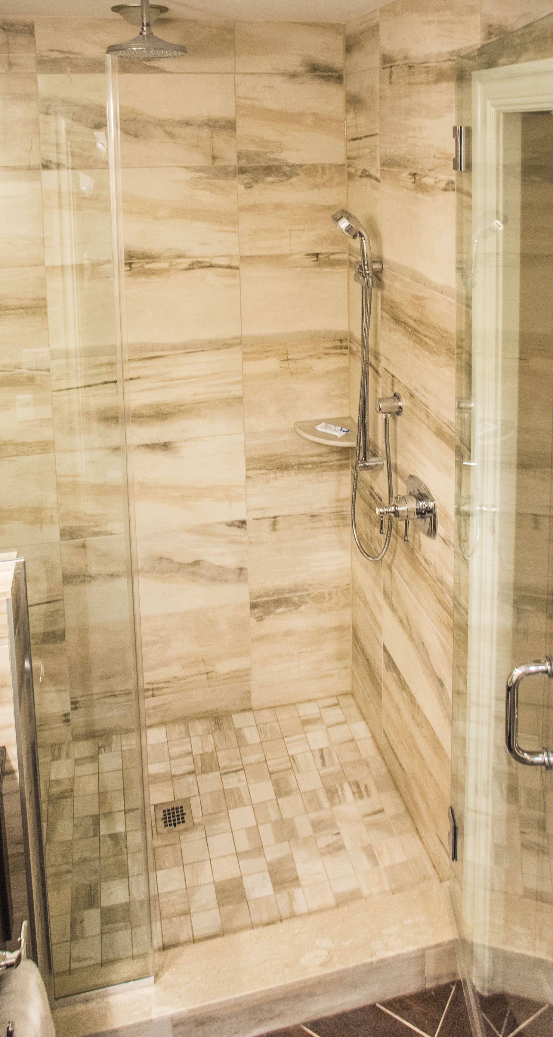 A glass-enclosed shower with a handheld showerhead and a wall-mounted faucet.