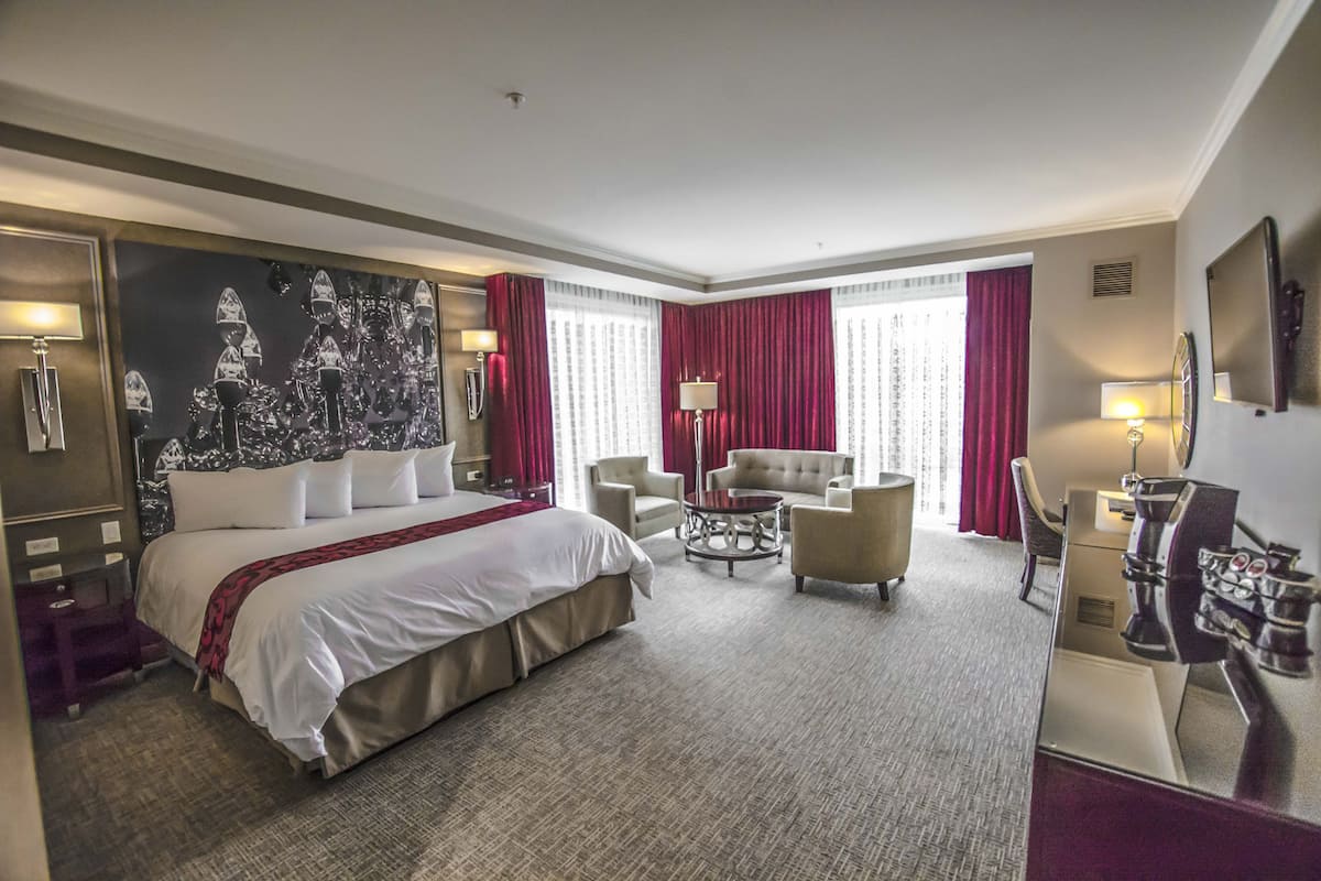 A hotel room with a large bed, two armchairs, a small table, and a desk with a lamp.