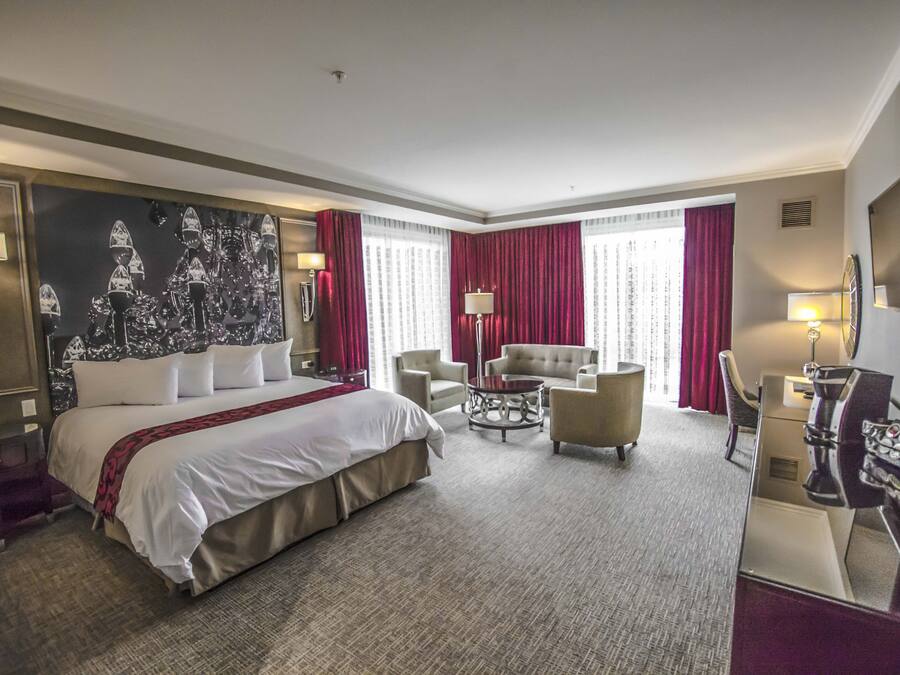 A hotel room with a large bed, two armchairs, a small table, and a desk with a lamp.