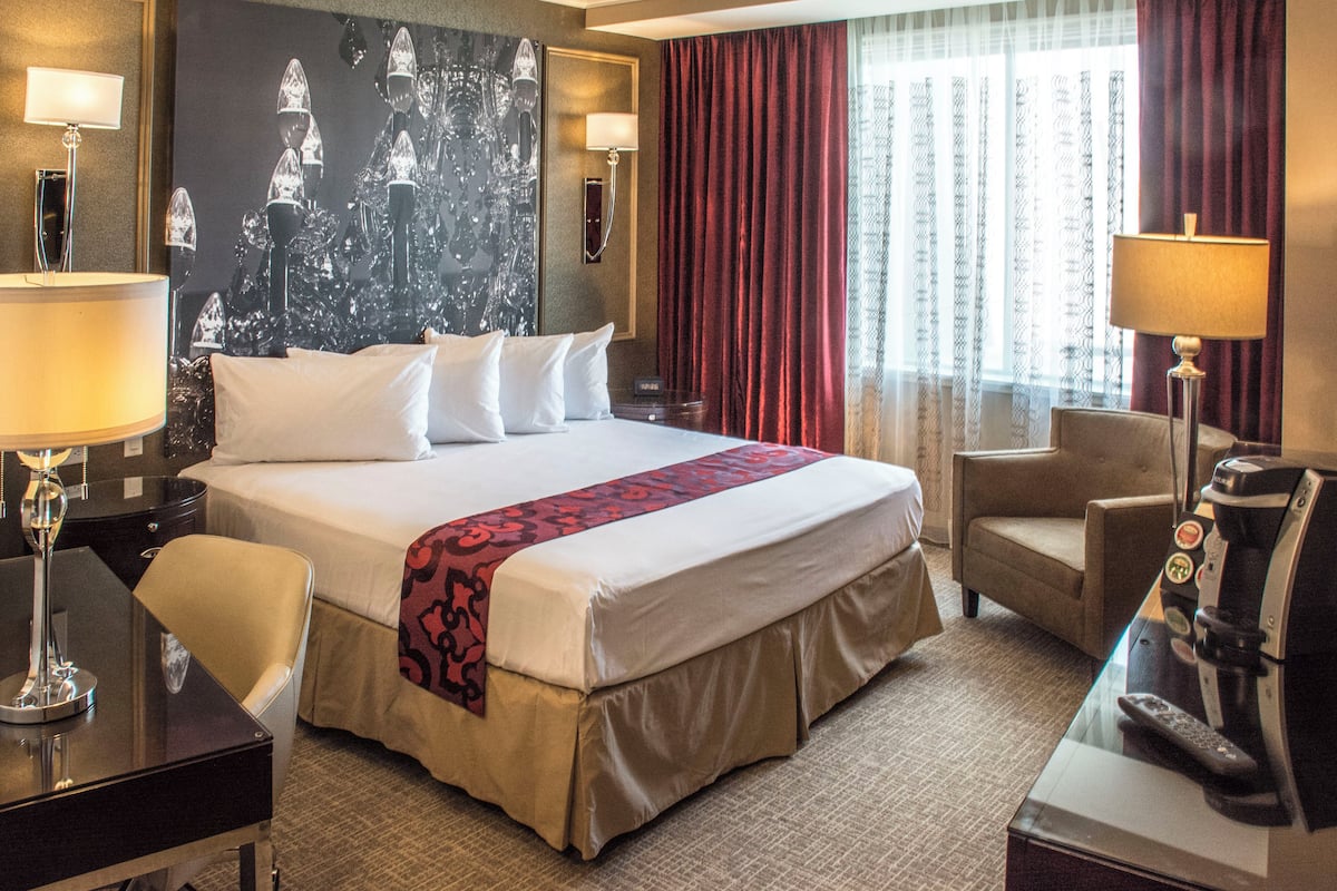 A hotel room with a large bed, two bedside tables, a desk with a lamp, a chair, and a coffee machine.