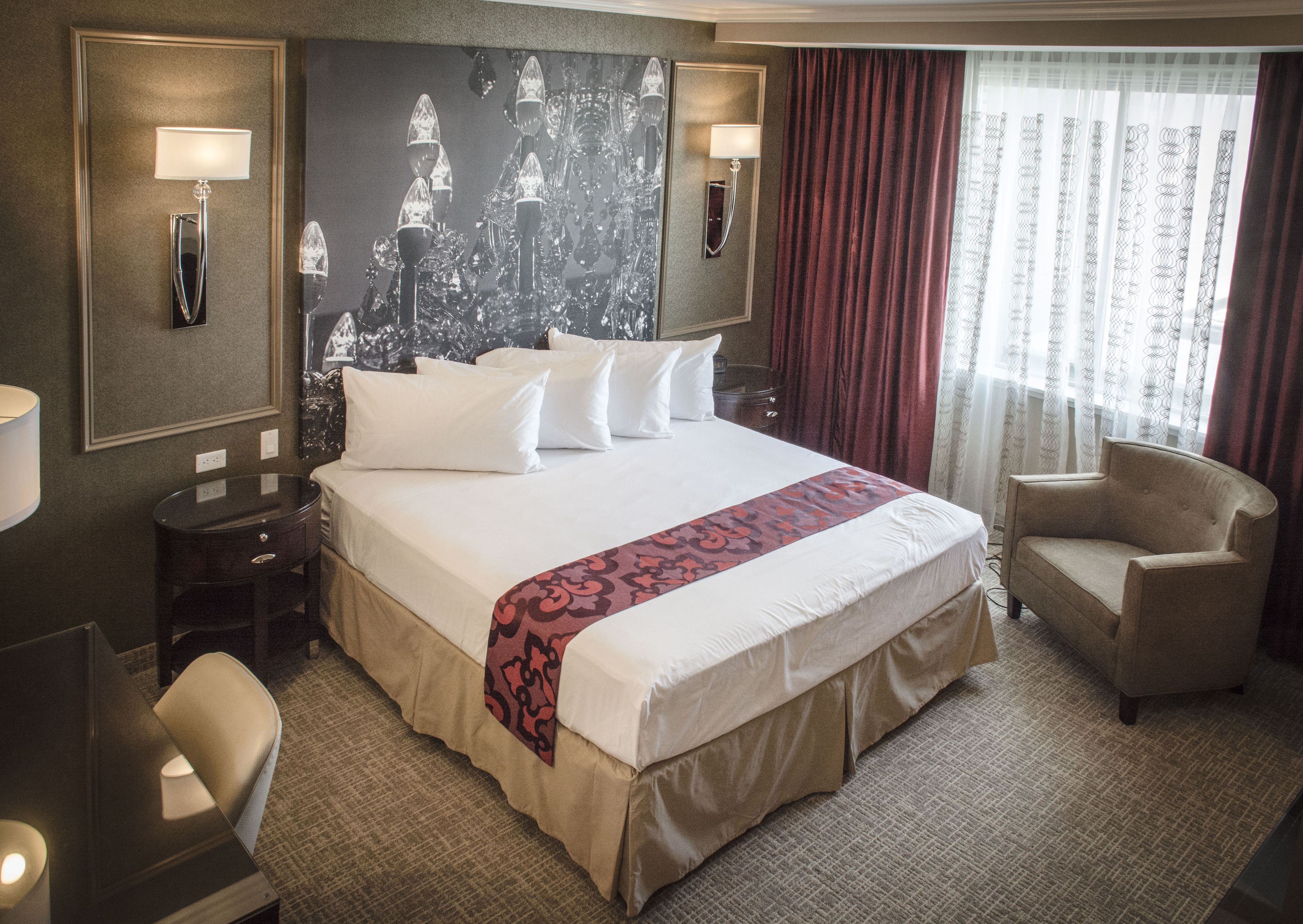 Camera d'hotel con un letto grande, due comodini, una sedia, una scrivania e un'ampia finestra con tende.