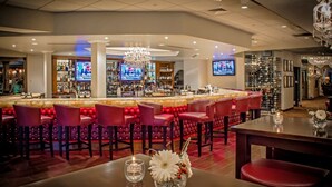 A bar area with red upholstered bar stools, a bar counter, and a chandelier. - The Delavan Hotel & Spa (Bowmansville)