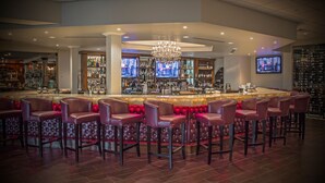 A bar area with leather barstools, a bar counter, and a television screen. - The Delavan Hotel & Spa (Bowmansville)
