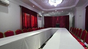 Uma sala de conferências com uma mesa comprida, cadeiras vermelhas e cortinas vermelhas.