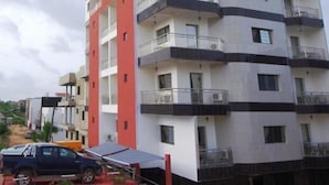 Um edifício residencial com vários andares e varandas, uma estátua no alto de uma colina e um caminhão estacionado.