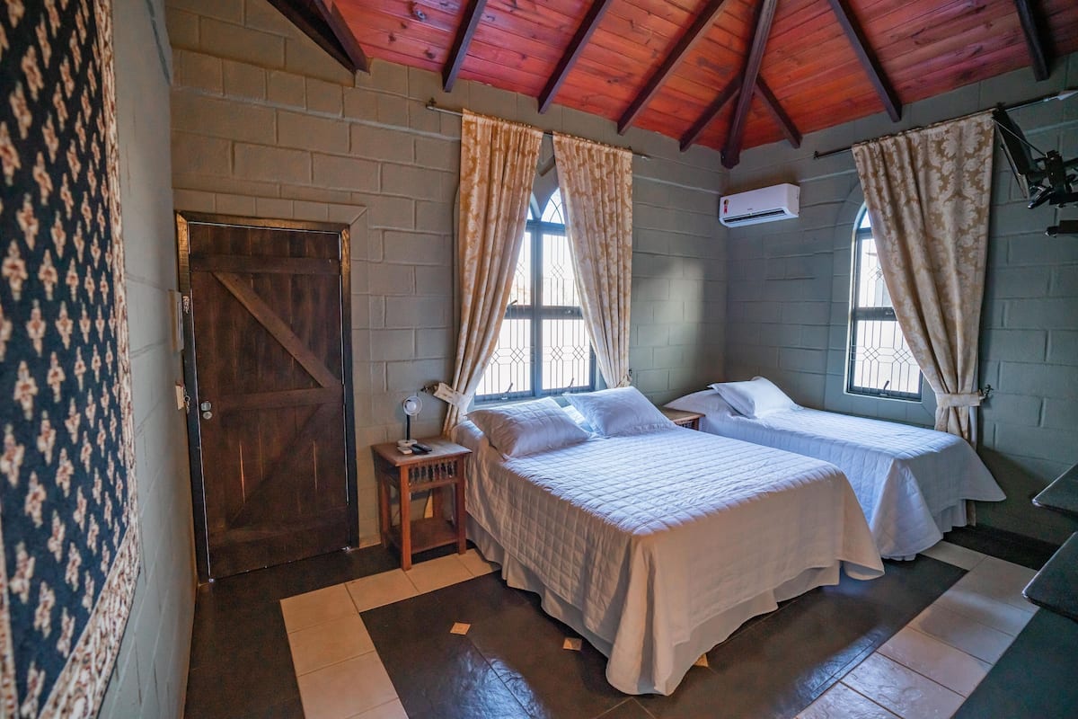 A bedroom with two beds, a wooden door, and a window with curtains.