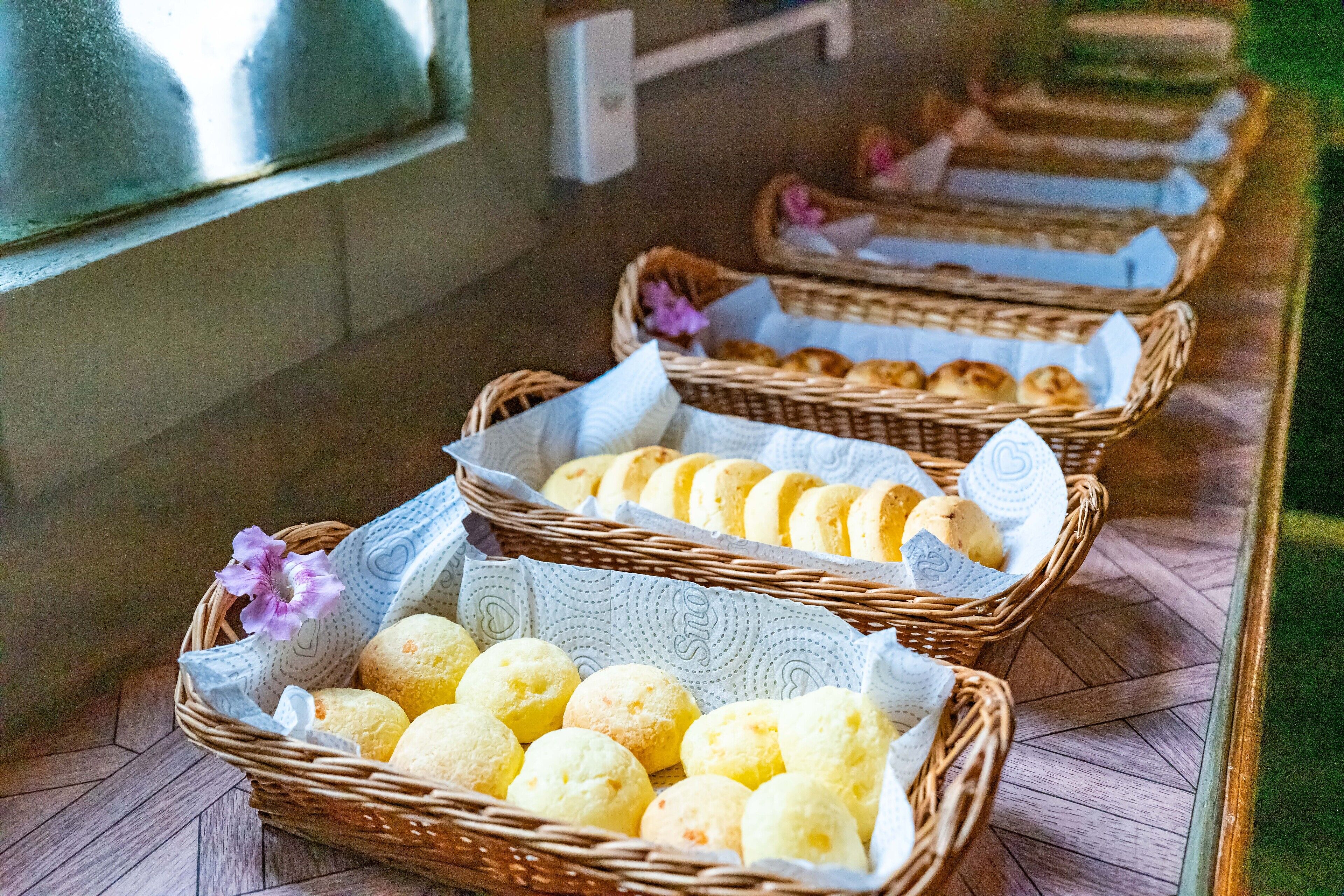 A row of wicker baskets filled with bread and pastries, arranged on a wooden floor.