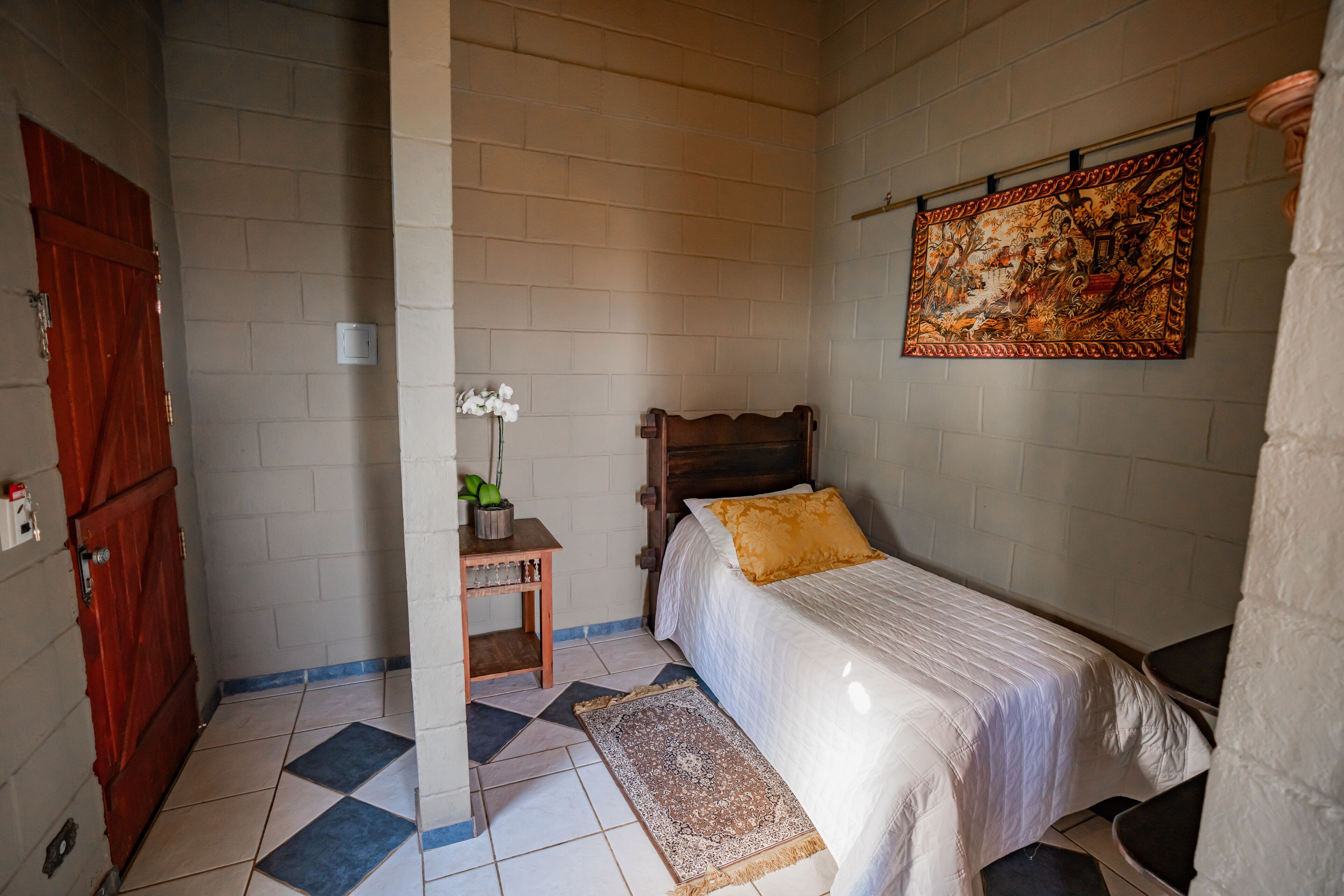 Un dormitorio con cama, mesita de noche, tapiz en la pared y puerta de madera.