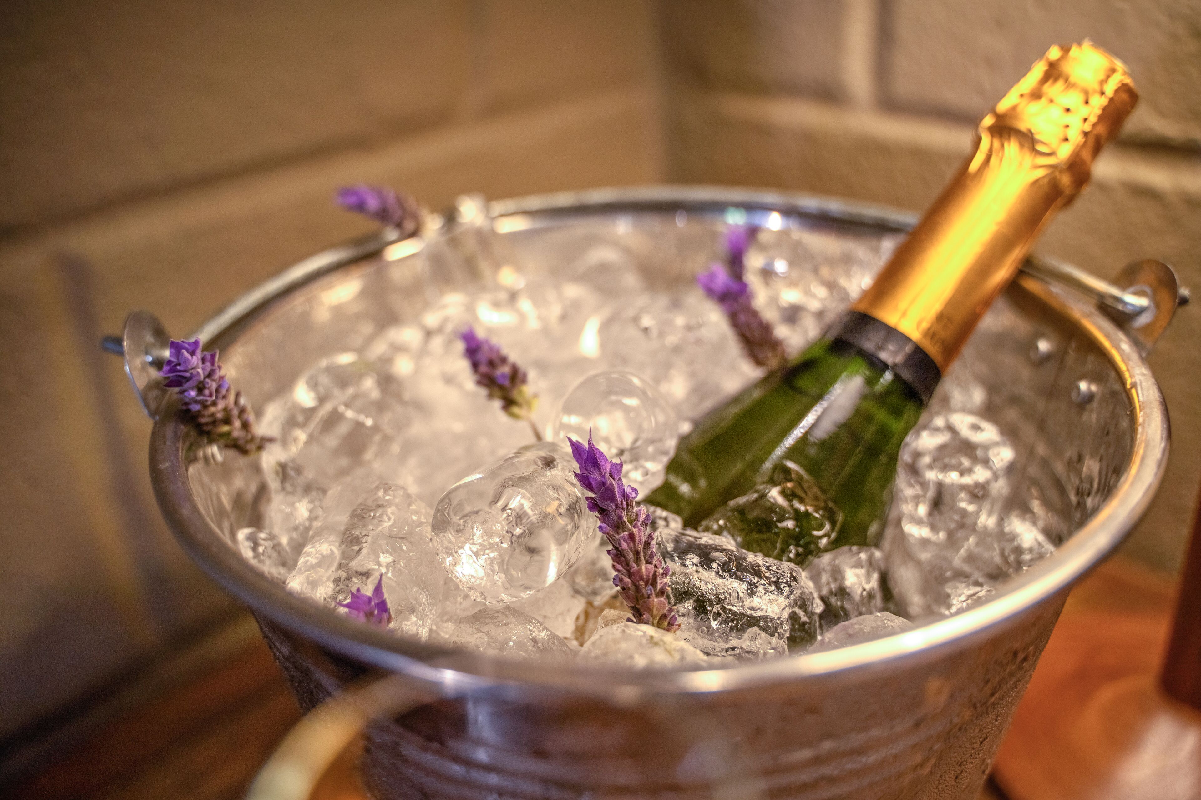 A champagne bottle in a metal bucket with ice and lavender sprigs.