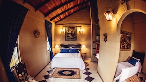 A bedroom with a large bed, two bedside tables, a nightstand, a small round table with a decorative item, and a patterned rug. - Pousada Camelot (Alto Paraíso de Goiás)