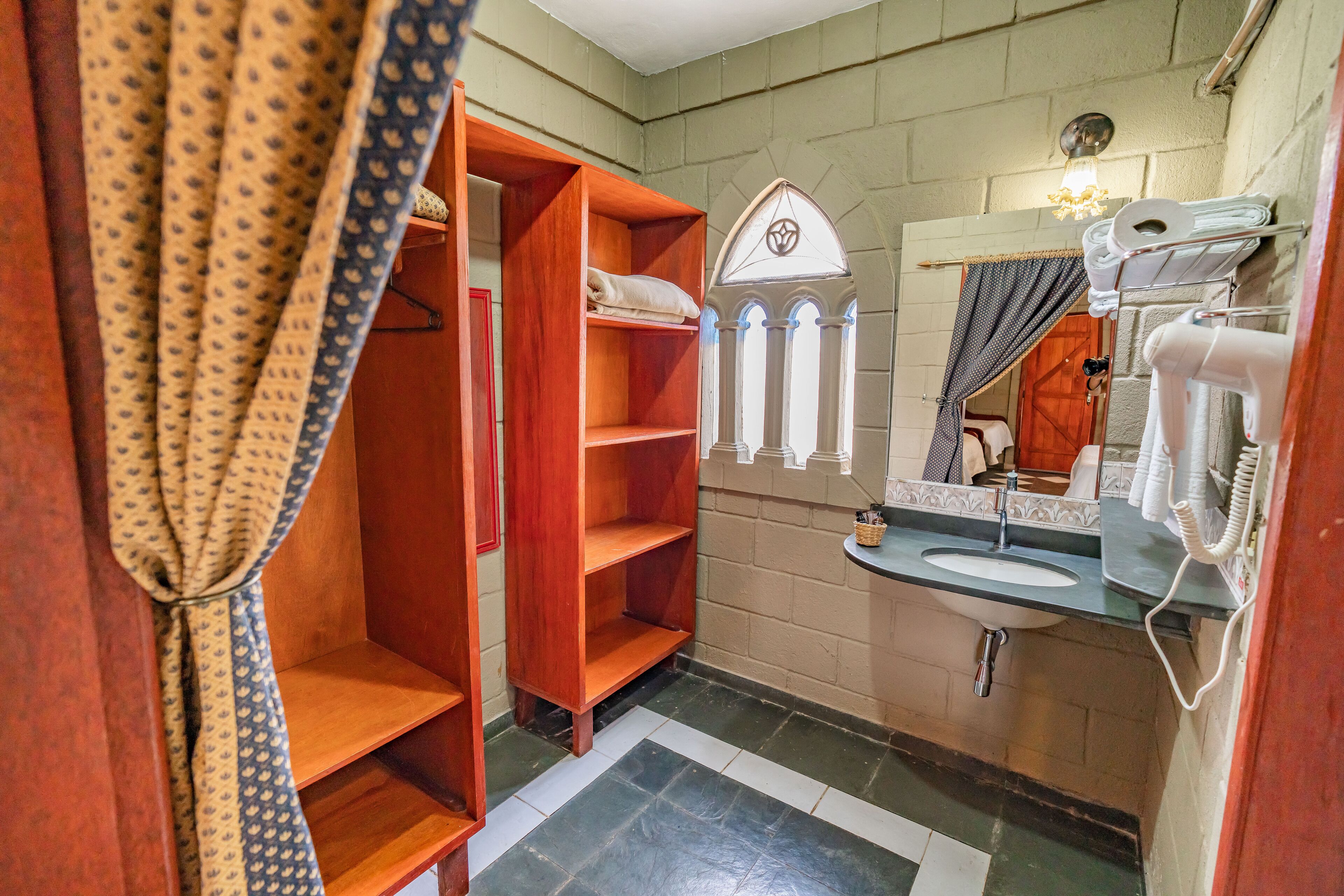 A bathroom with a wooden shelf unit, a sink with a mirror, and a towel rack.