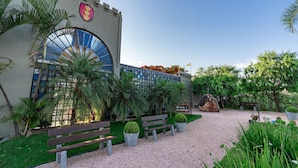 A courtyard with benches, palm trees, and a building with a large arched window. - Pousada Camelot (Alto Paraíso de Goiás)