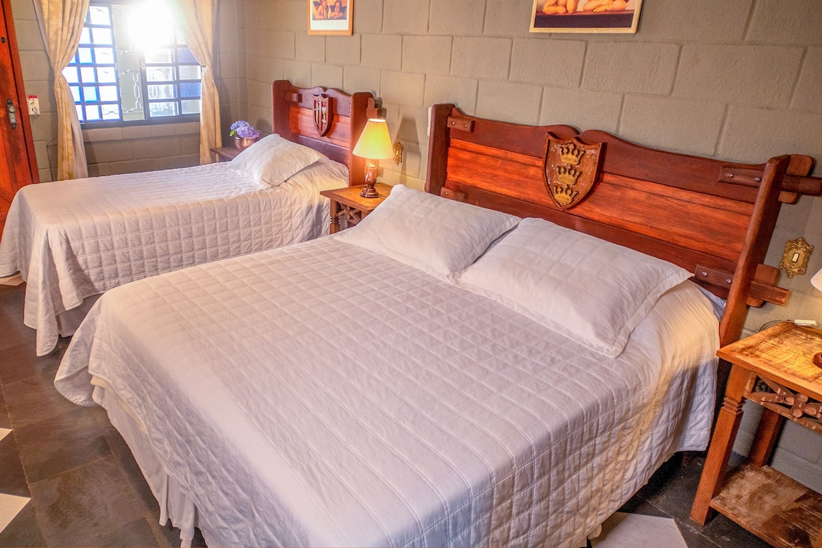 A room with two beds, a wooden headboard, a nightstand with a lamp, and a checkered floor.