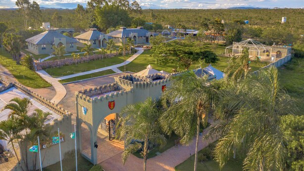 A castle-like structure with a central tower, surrounded by lush greenery and palm trees. - Pousada Camelot (Alto Paraíso de Goiás)