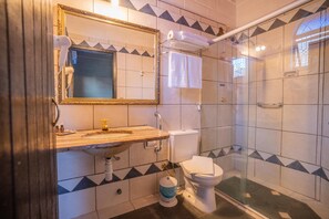 Compact bathroom with a large mirror, wooden vanity, and modern toilet, featuring a geometric tile pattern and glass-enclosed shower.