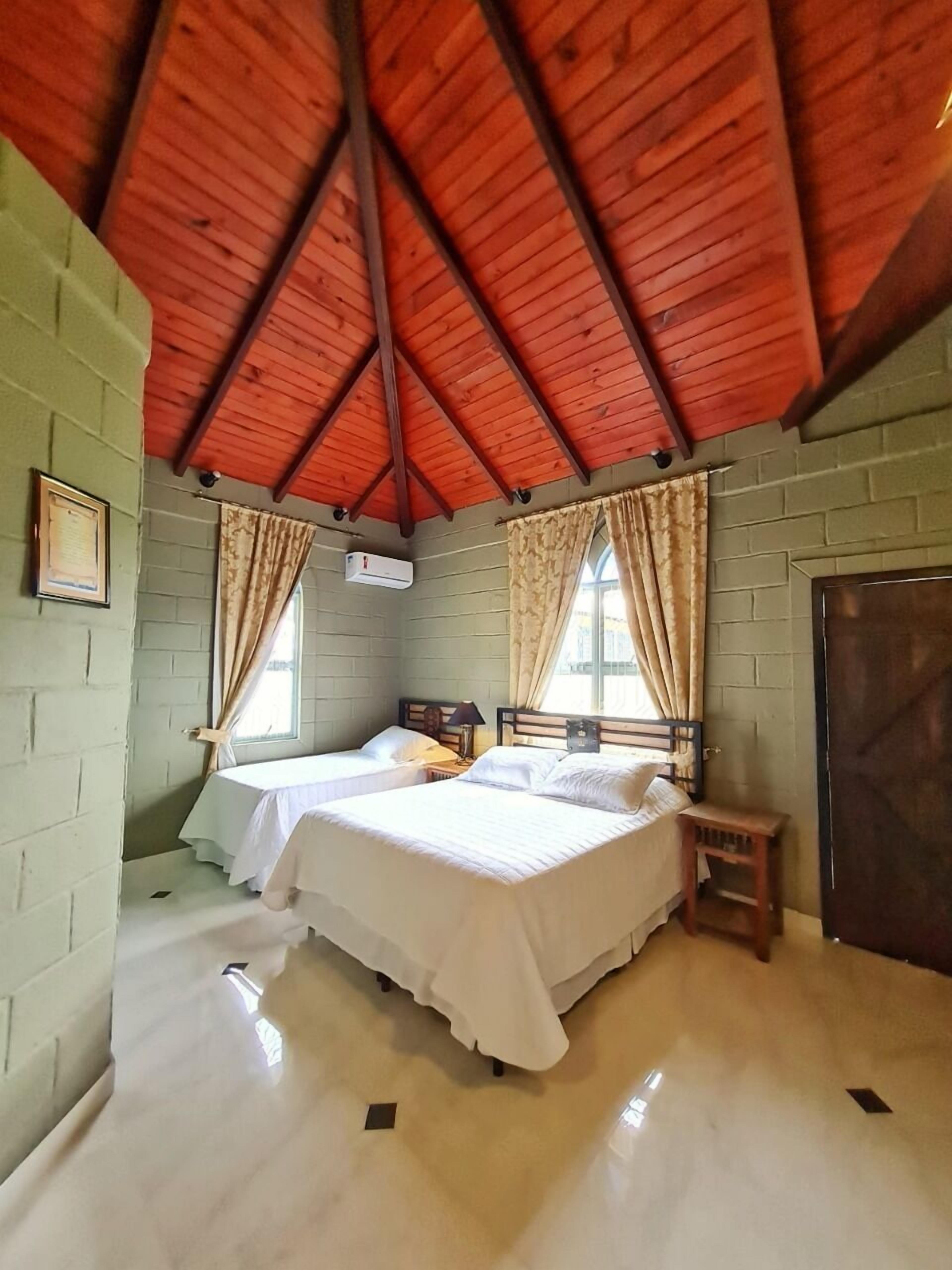 A room with two beds, a wooden ceiling, and a brick wall.