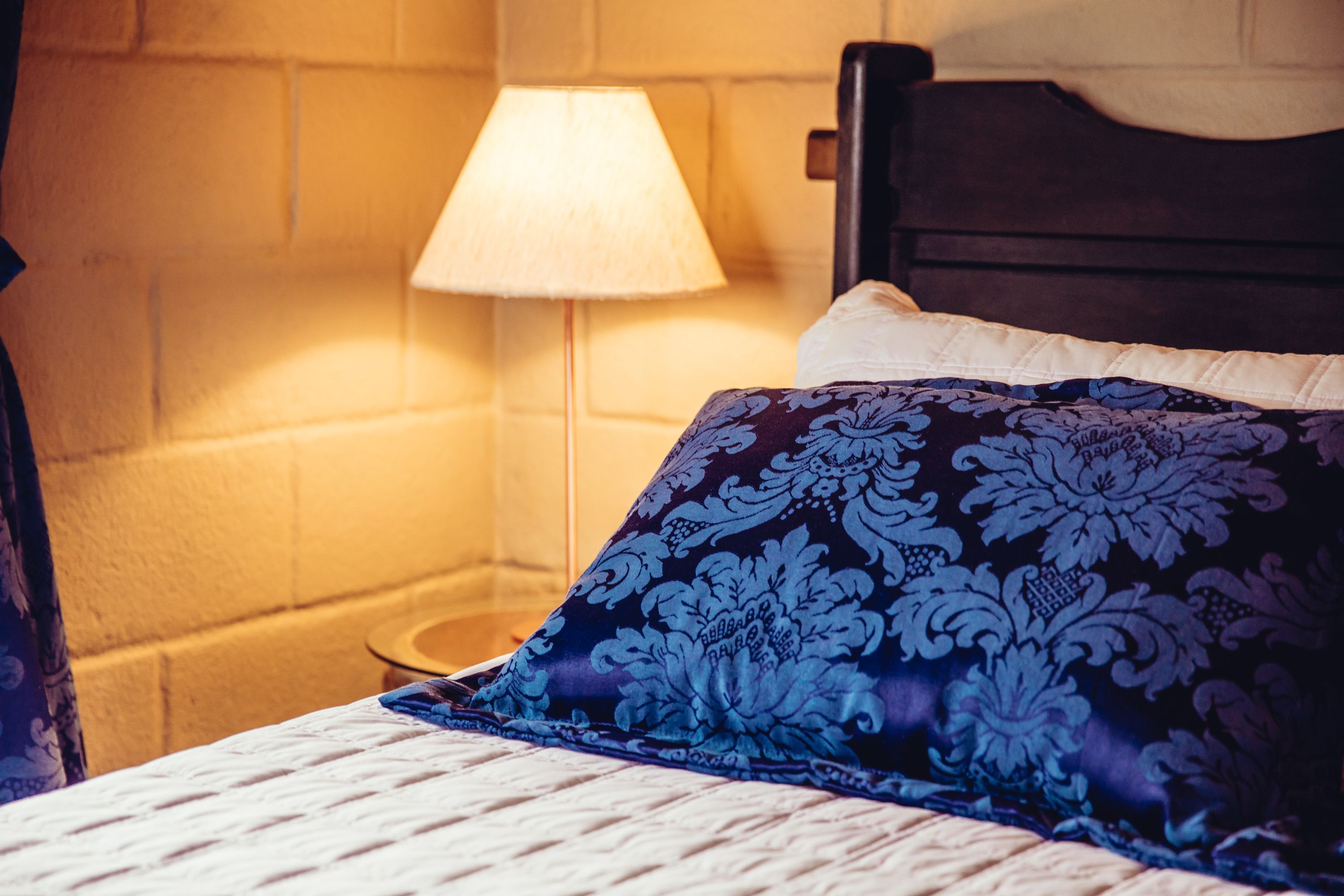 A neatly made bed with a patterned pillow and a bedside lamp.