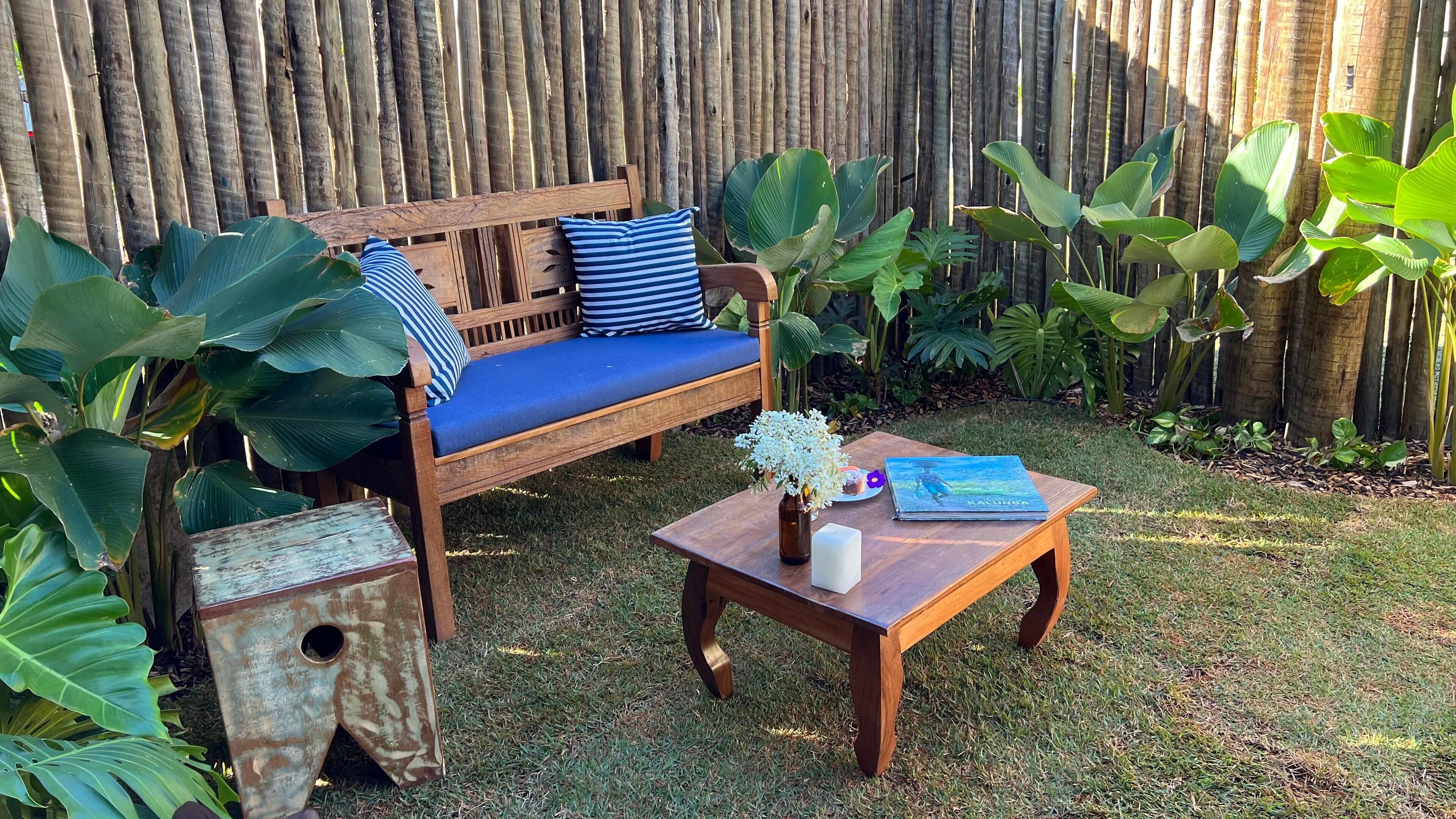 A wooden bench with blue cushions and a small table with a book and a vase of flowers.