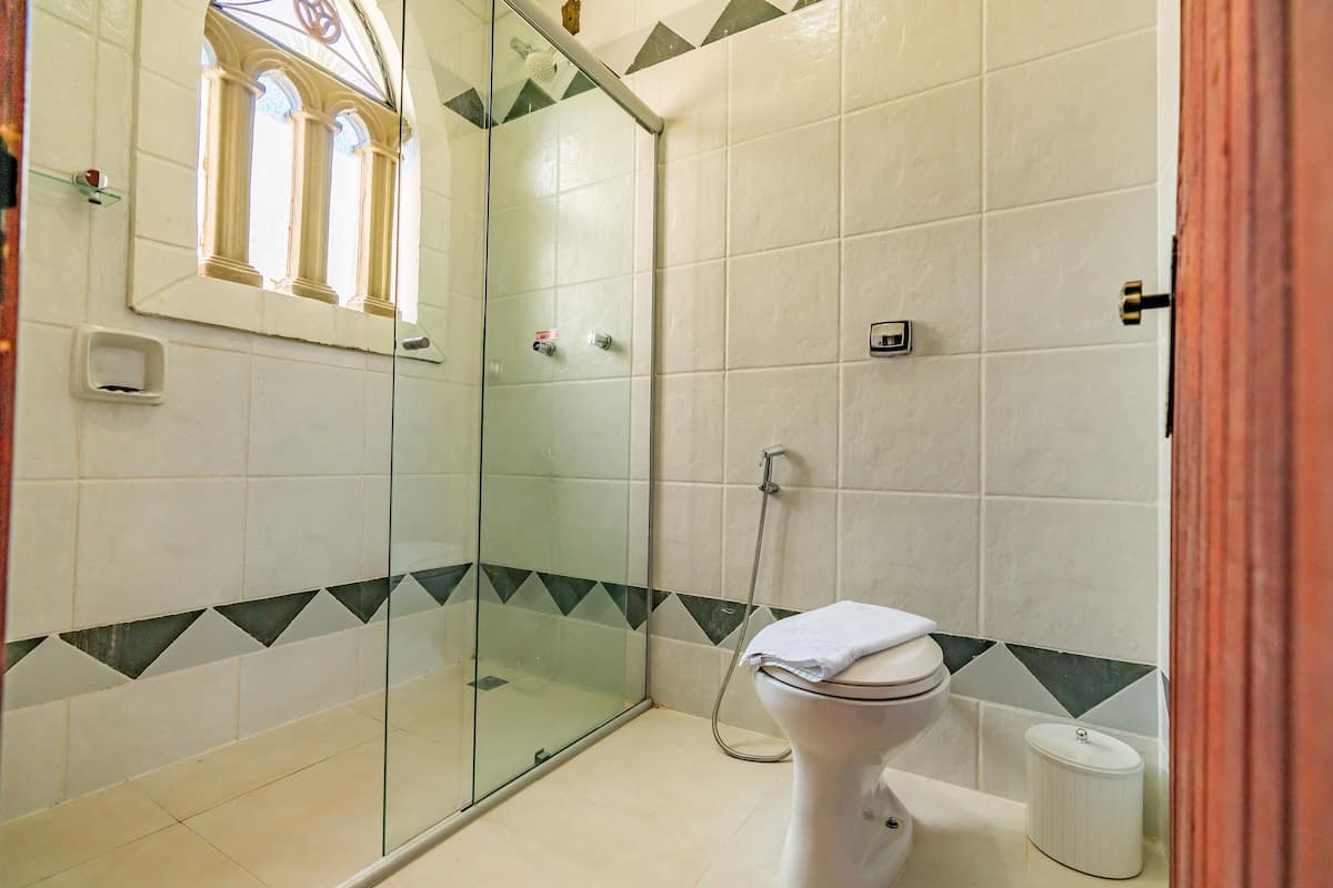 A bathroom with a glass-enclosed shower, a toilet, and a small window with a decorative frame.