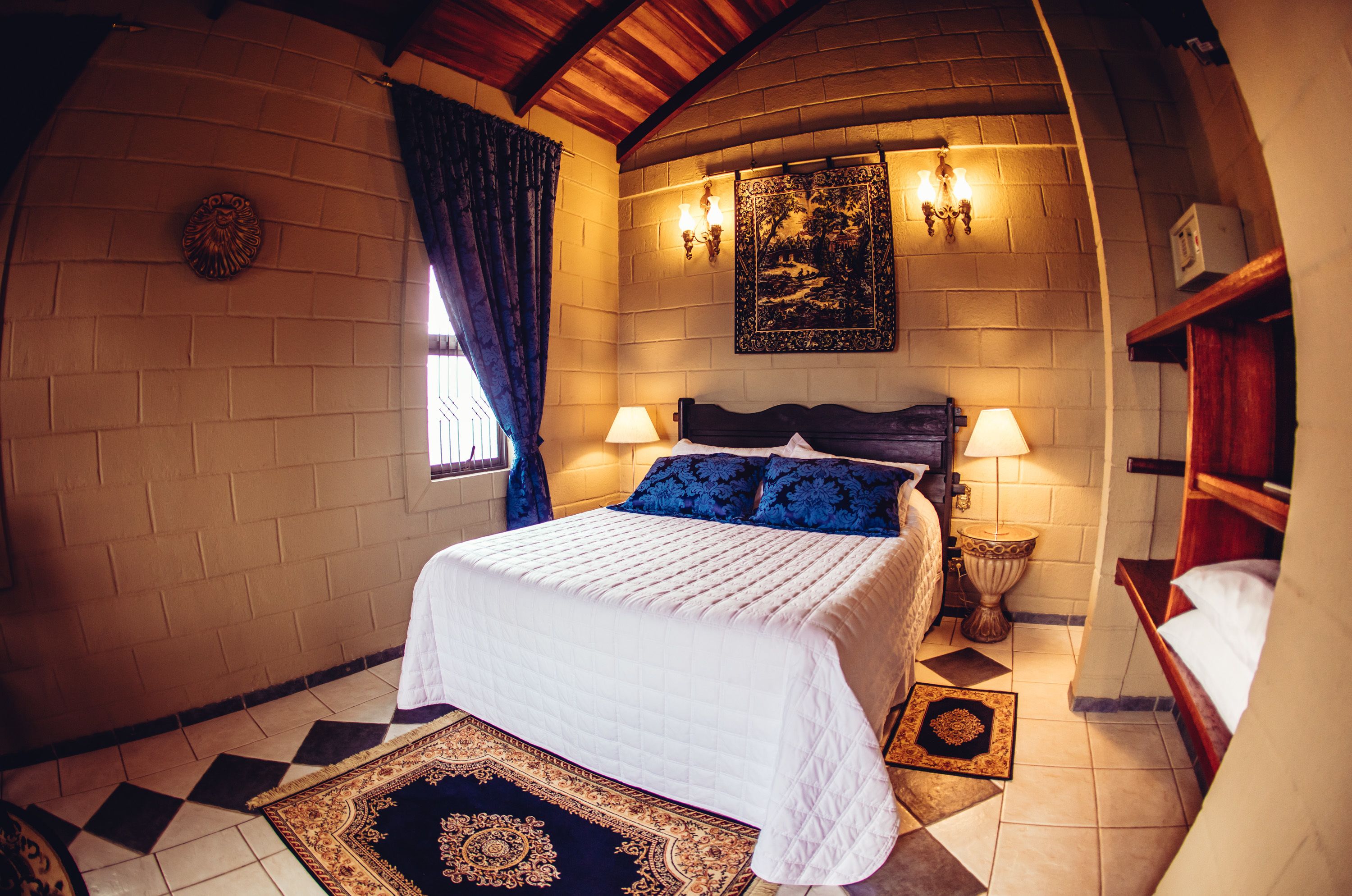 A bedroom with a large bed, two bedside lamps, a decorative rug, and a wall-mounted picture.