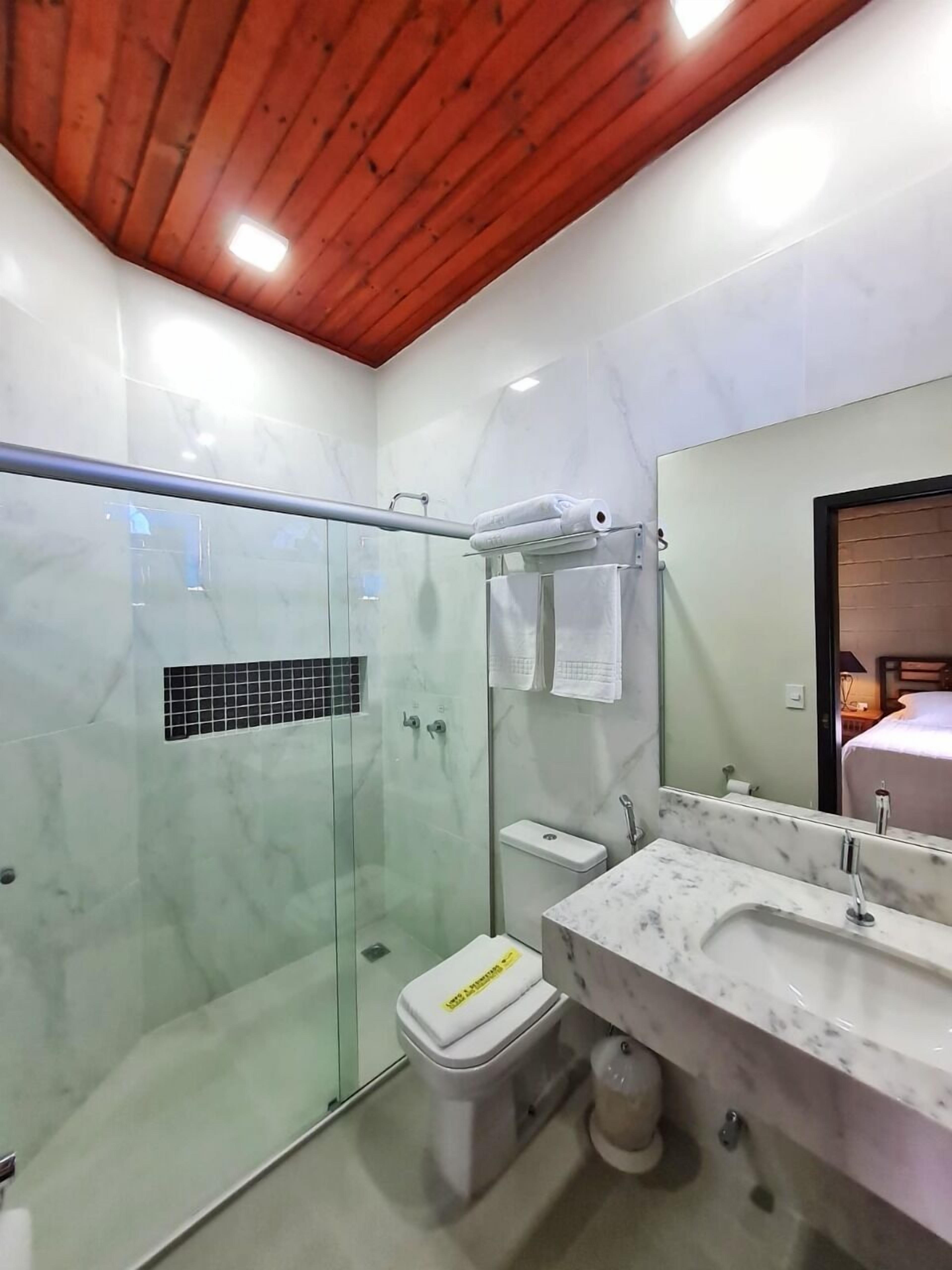 A modern bathroom with a glass-enclosed shower, a marble sink, and a wooden ceiling.