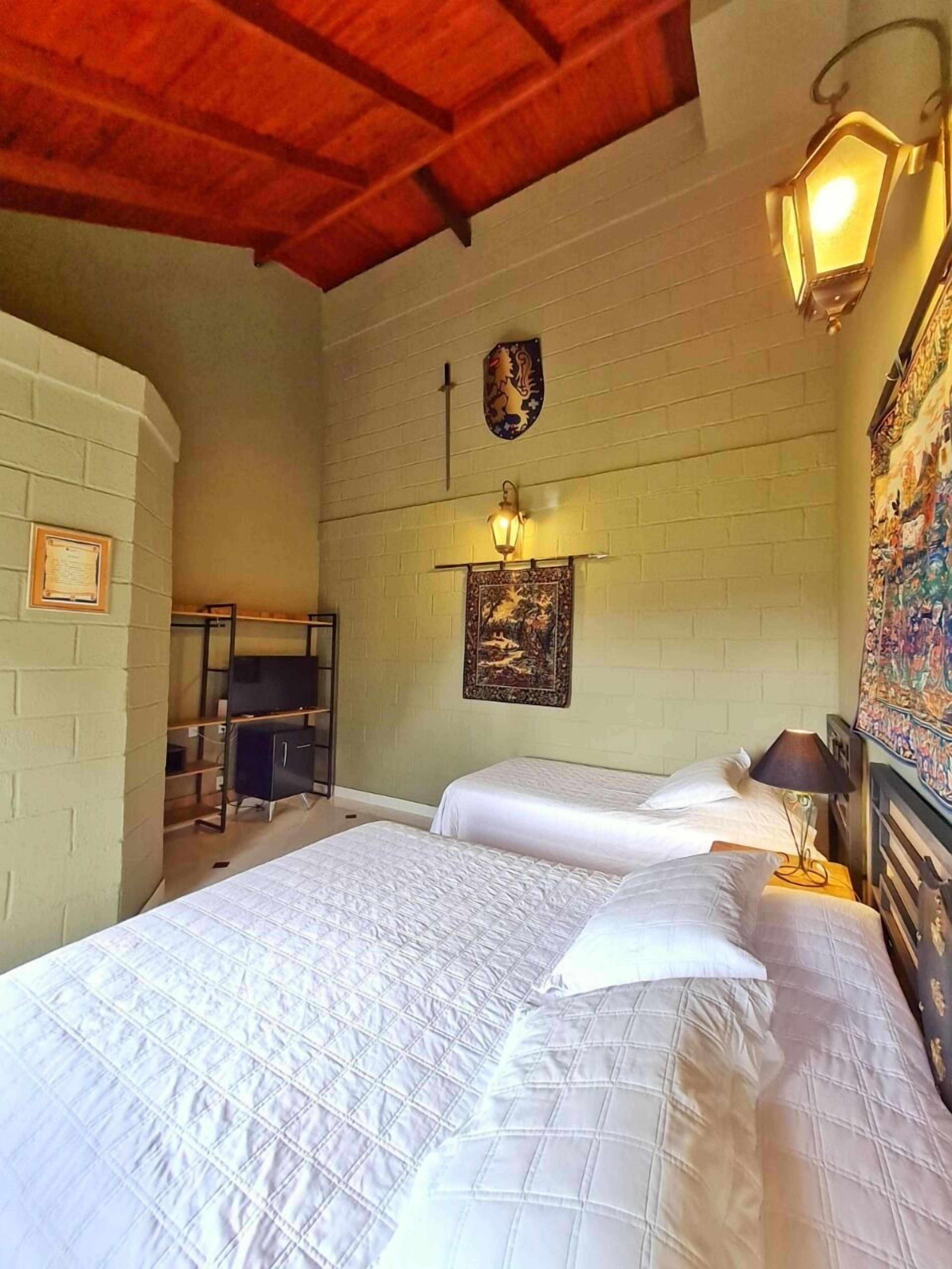 Habitación con dos camas, techo de madera, lámpara de pared y un escudo decorativo.