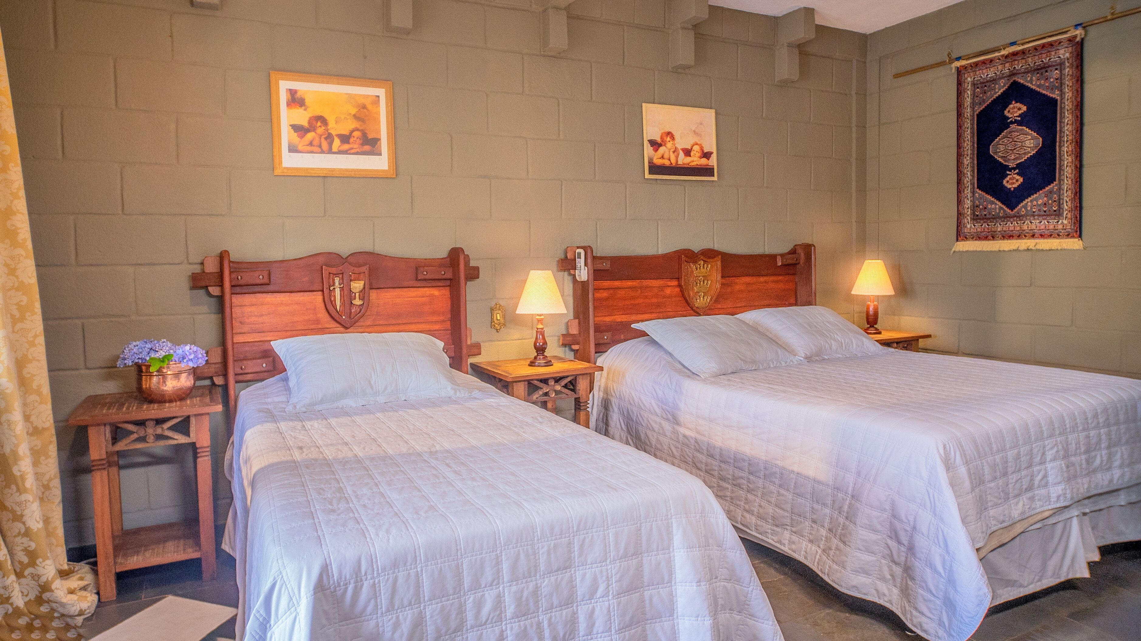 Ein Zimmer mit zwei Einzelbetten, Holz-Kopfteilen, Nachttischen mit Lampen und einer Wand mit zwei gerahmten Bildern.