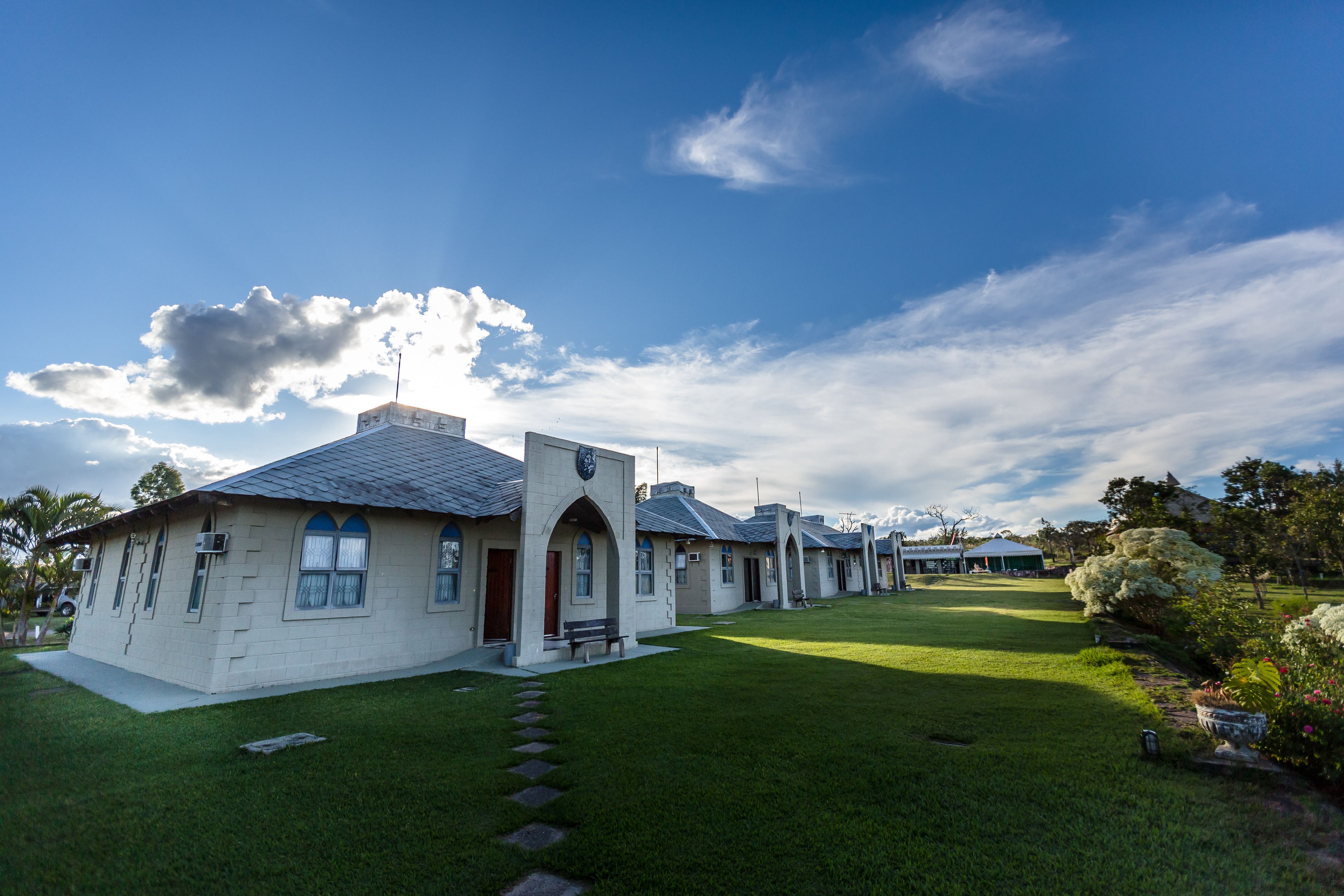 A row of white buildings with a central arched entrance, surrounded by a well-maintained lawn and trees.
