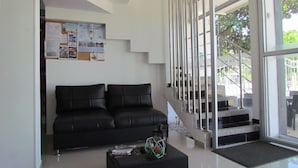 Un vestíbulo moderno con un sofá de cuero negro, una mesa de centro con revistas y una escalera que lleva a un área exterior.