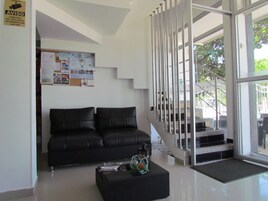 Un vestíbulo moderno con un sofá de cuero negro, una mesa de centro con revistas y una escalera que lleva a un área exterior.
