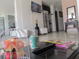Una sala de estar moderna con una mesa de centro de vidrio, un sofá blanco, un mueble negro y un televisor instalado en la pared.