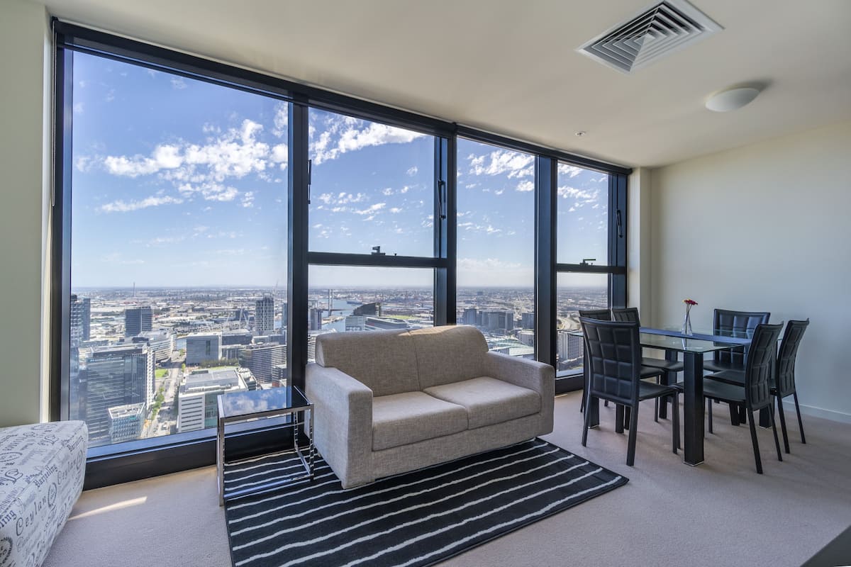 A modern living room with a large window, a sofa, a dining table with chairs, and a city view.