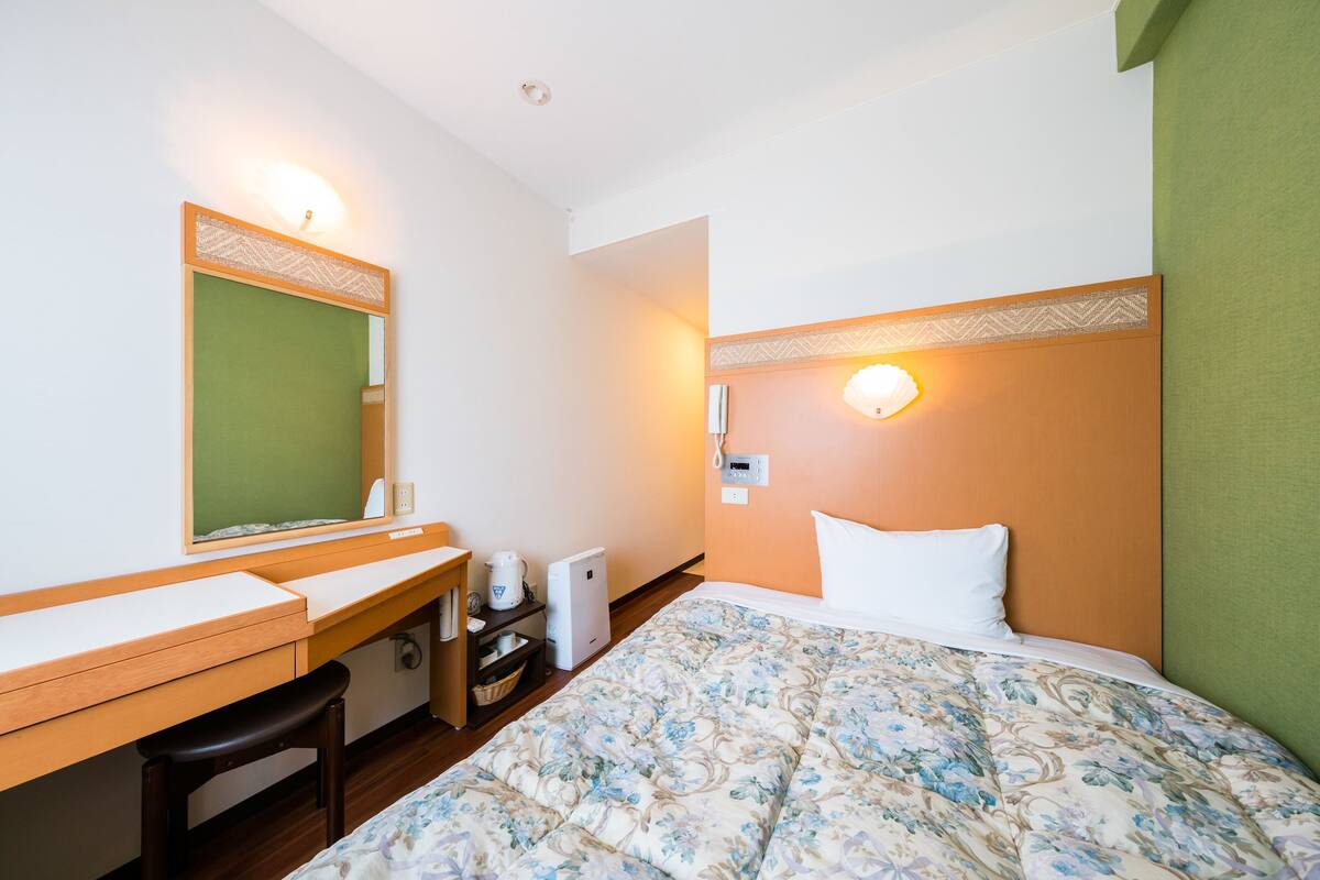 Ein Hotelzimmer mit einem Bett, einem Schreibtisch, einem Stuhl, einem Spiegel, einem Nachttisch und einer Wandlampe.