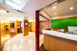 A hotel reception area with a reception desk, a green acoustic panel, and a wooden floor.