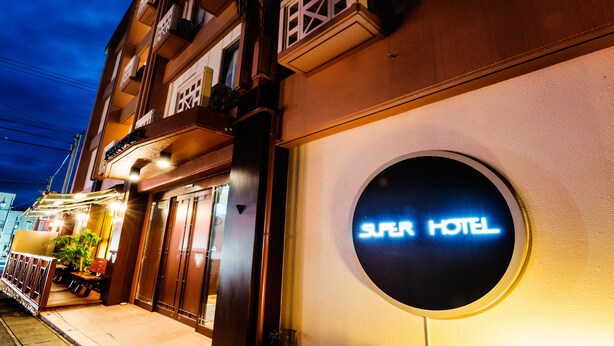 L’entrée d’un hôtel, avec une enseigne indiquant « Super Hôtel » et une porte d’entrée bien visible.