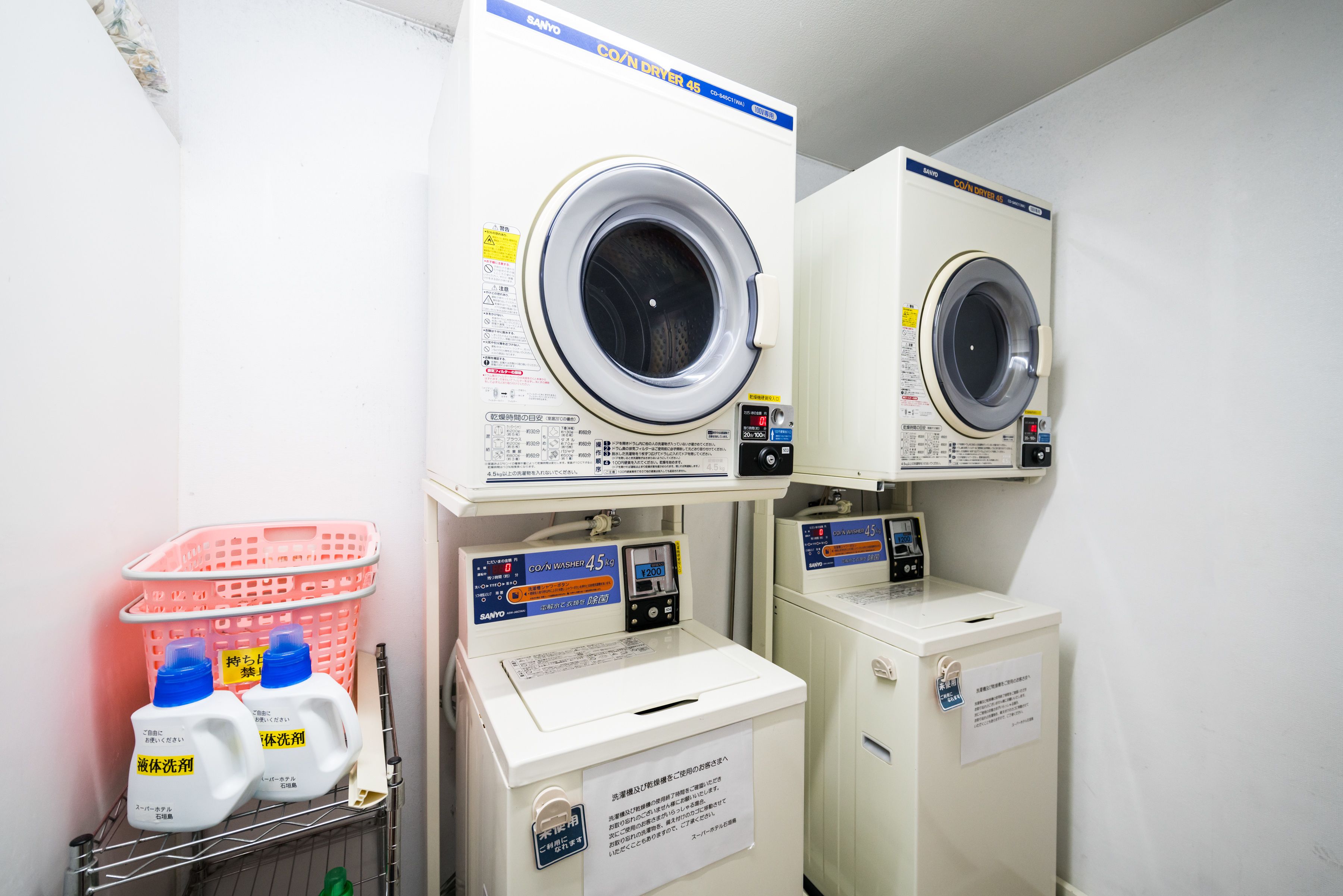A laundry room with two front-loading washing machines, a pink basket, and detergent bottles.