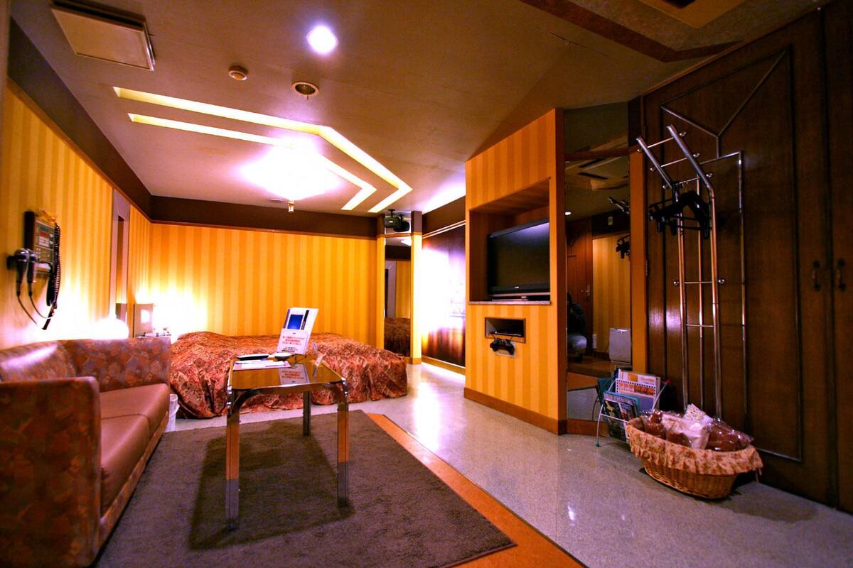 A hotel room with a sofa, a small table, a television, and a bathroom with a shower and a towel rack.