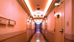 Een hotelgangen met genummerde deuren, een spiegelende vloer en een plafond met inbouwverlichting.