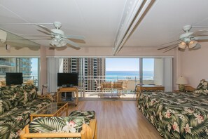 A spacious room with a balcony, a TV, and a bed with tropical floral bedding.