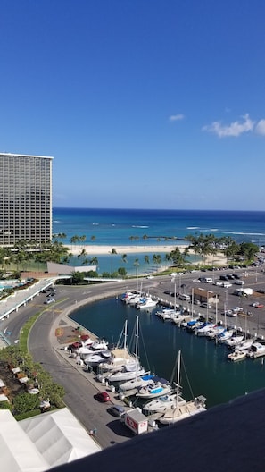 A marina with boats docked, a beach, and a tall hotel building in the background.