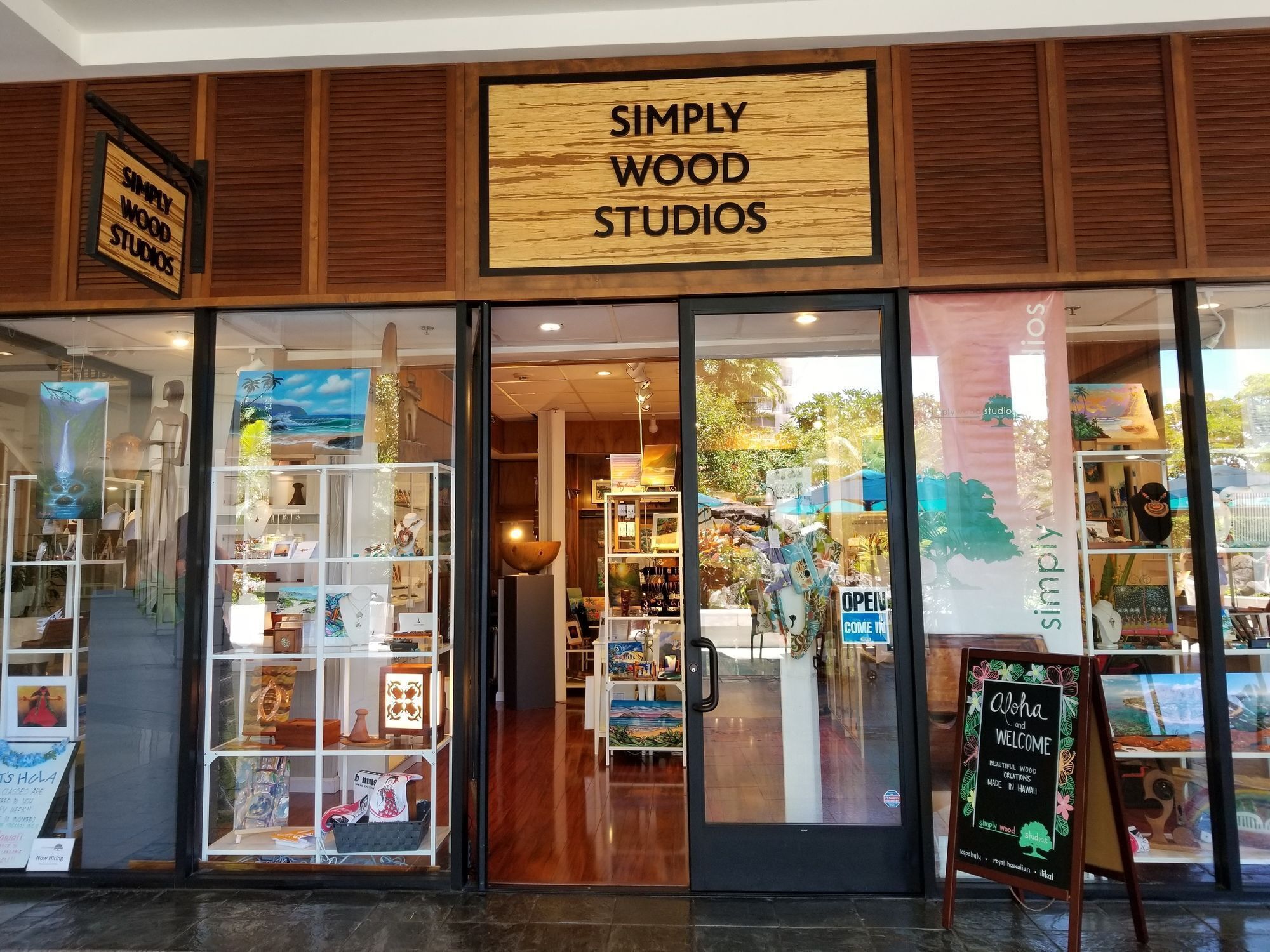 Ein Schaufenster mit einem Schild, auf dem "Simply Wood Studios" steht, und Glastüren, die verschiedene Holzprodukte präsentieren.