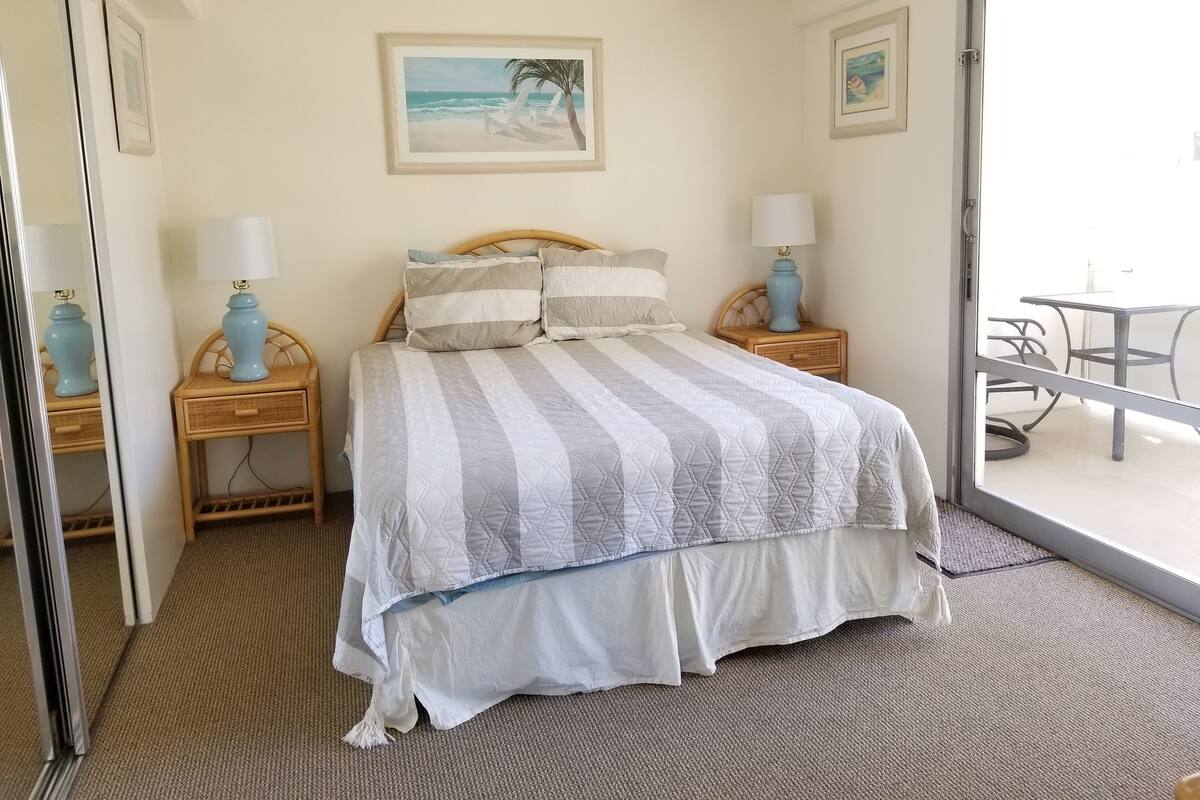 A neatly made bed with striped bedding, two bedside tables with lamps, and a view of an outdoor patio area.