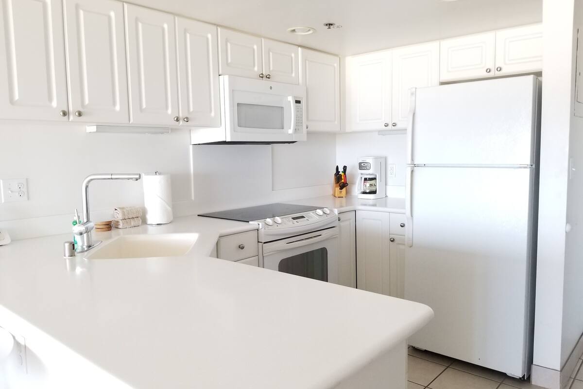 A modern kitchen with white cabinetry, a stainless steel refrigerator, a microwave, an oven, and a coffee maker.