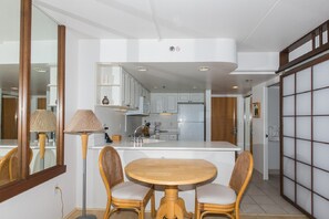 A modern kitchen with white cabinets, a central island, and a dining area with wicker chairs.